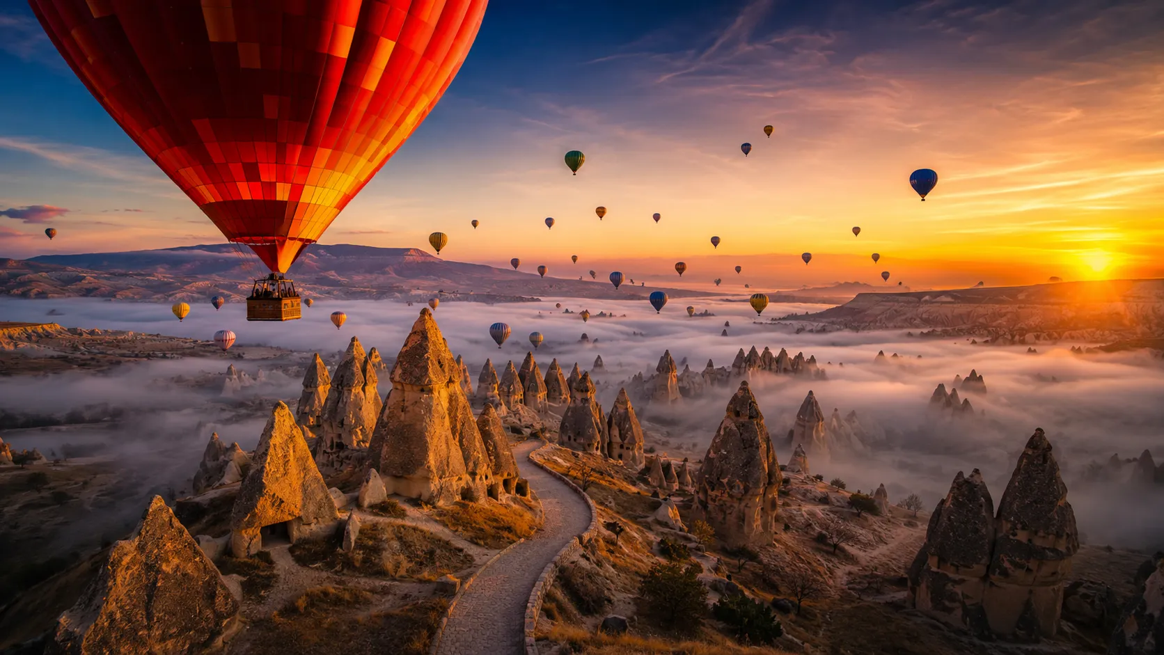 Dozens of colorful hot-air balloons rise over Cappadocia's fairy chimneys at golden sunrise, with morning mist blanketing the valley the iconic highlight of a Turkey family trip planned through Zaviamo.