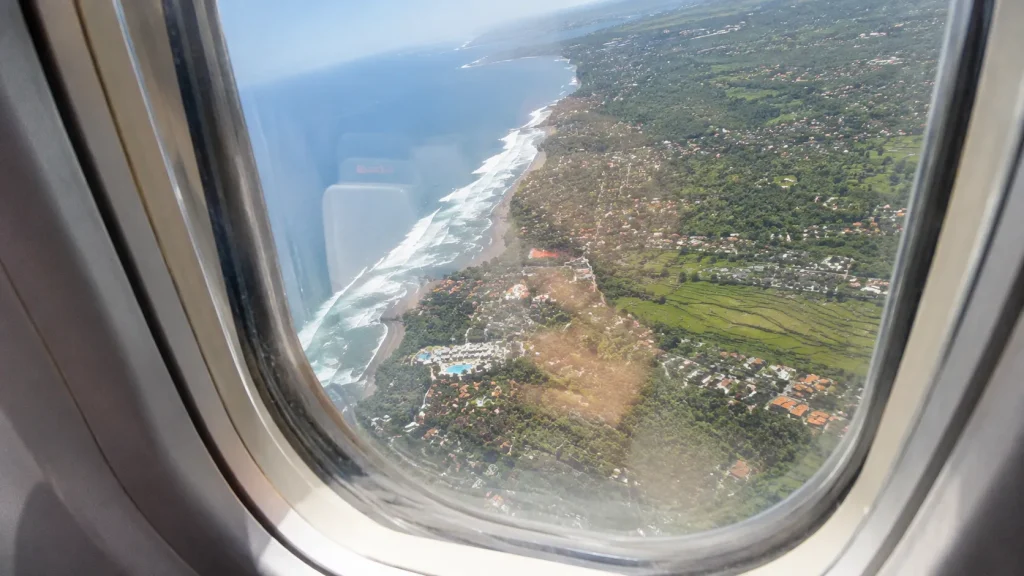 Aerial view of Bali's green rice paddies and Indian Ocean coastline photographed through a scratched airplane window at midday