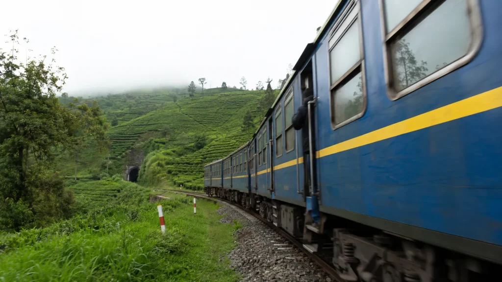 Sri Lanka Railways train moving through terraced emerald tea estates in the misty central highlands near Ella | Sri Lanka Sustainable Travel