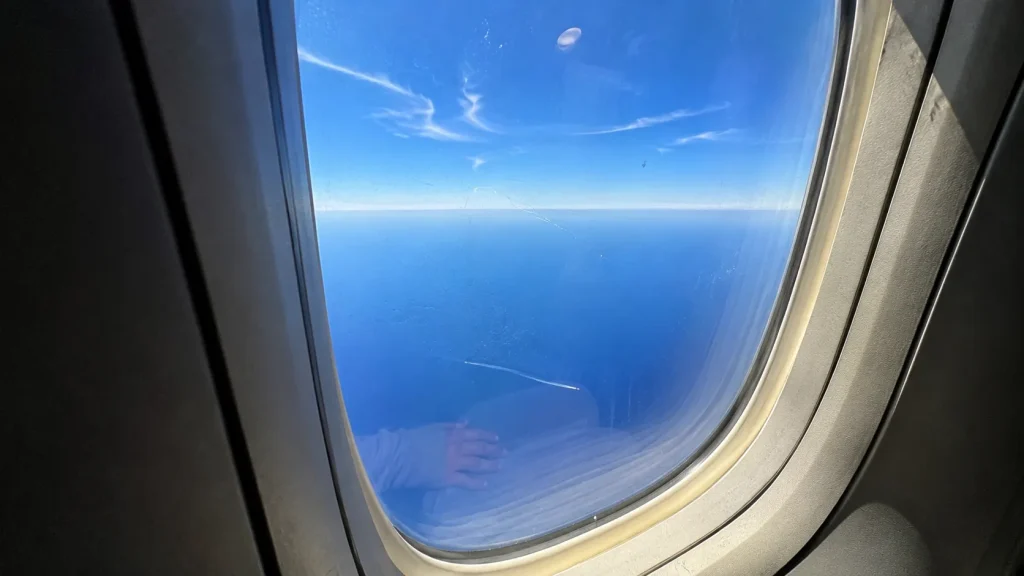 View through scratched airplane window at brilliant blue Indian Ocean below on a short daytime flight to Colombo