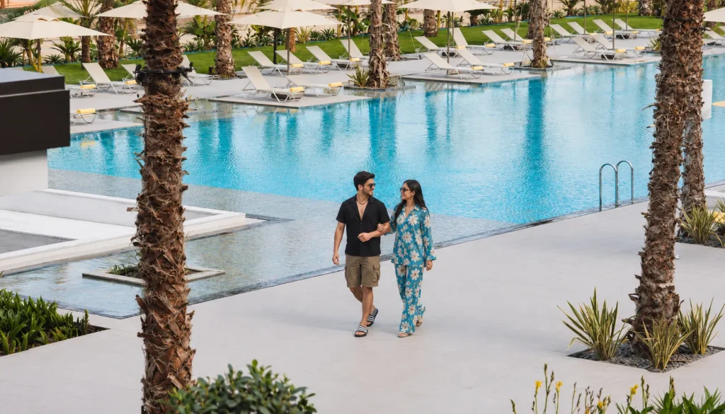 Couple walking beside resort infinity pool with sun loungers, Turkey wellness retreats resort stay