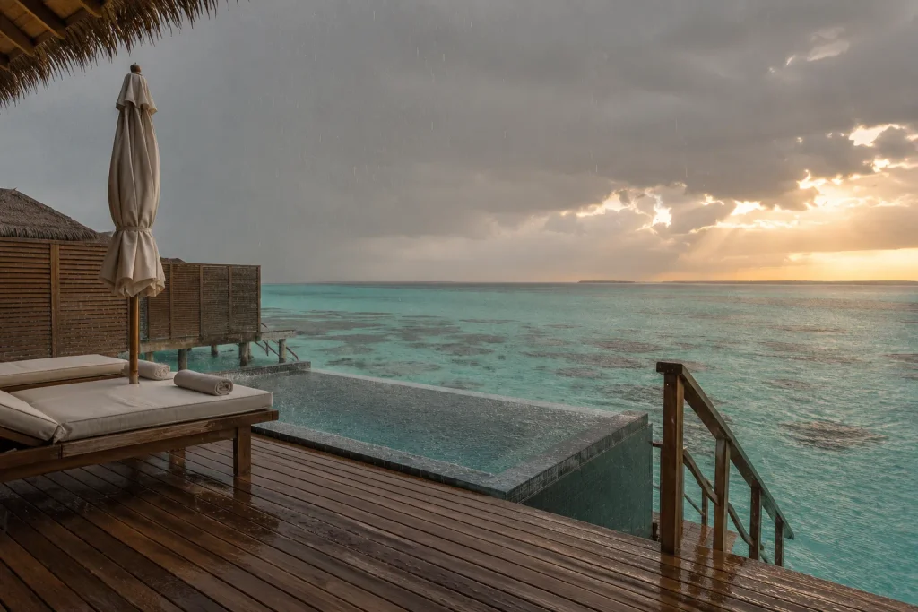 Overwater villa in the Maldives during a September shoulder-season rain shower, with sunset breaking through.