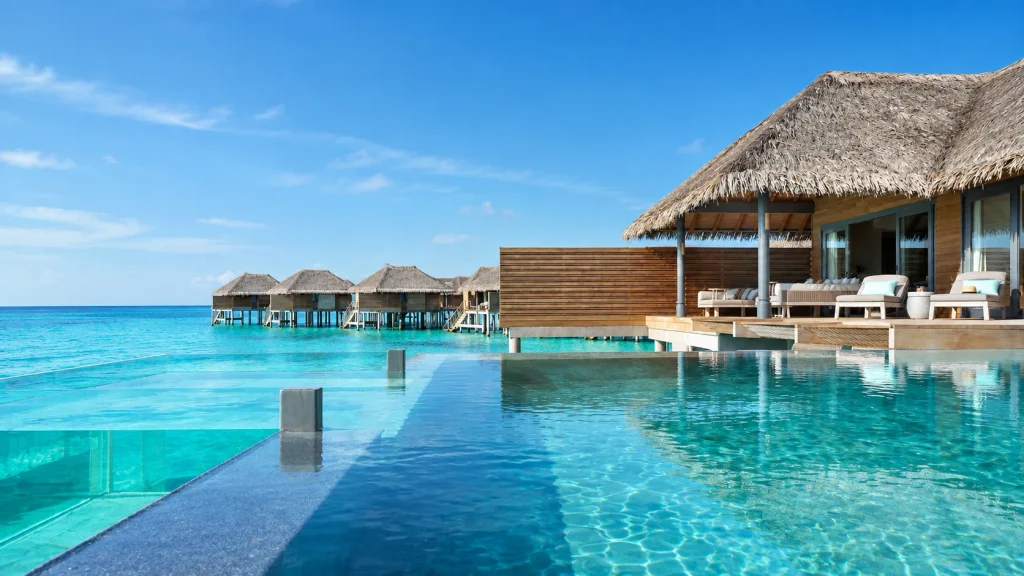 Glass-bottom infinity pool walkway leading toward a row of thatched Maldives Overwater Pool Villas