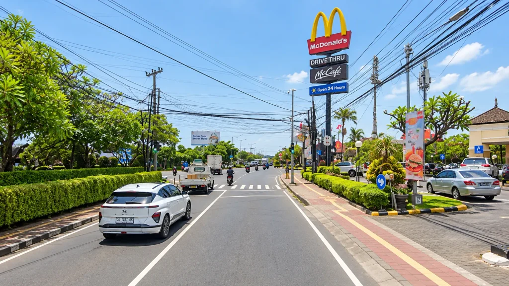Busy southern Bali road with motorbikes, power lines and roadside shops, the traffic a package itinerary drives through