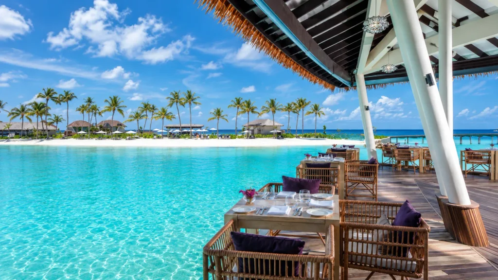 Rattan dining tables on an overwater deck facing a turquoise lagoon at a halal Maldives resorts
