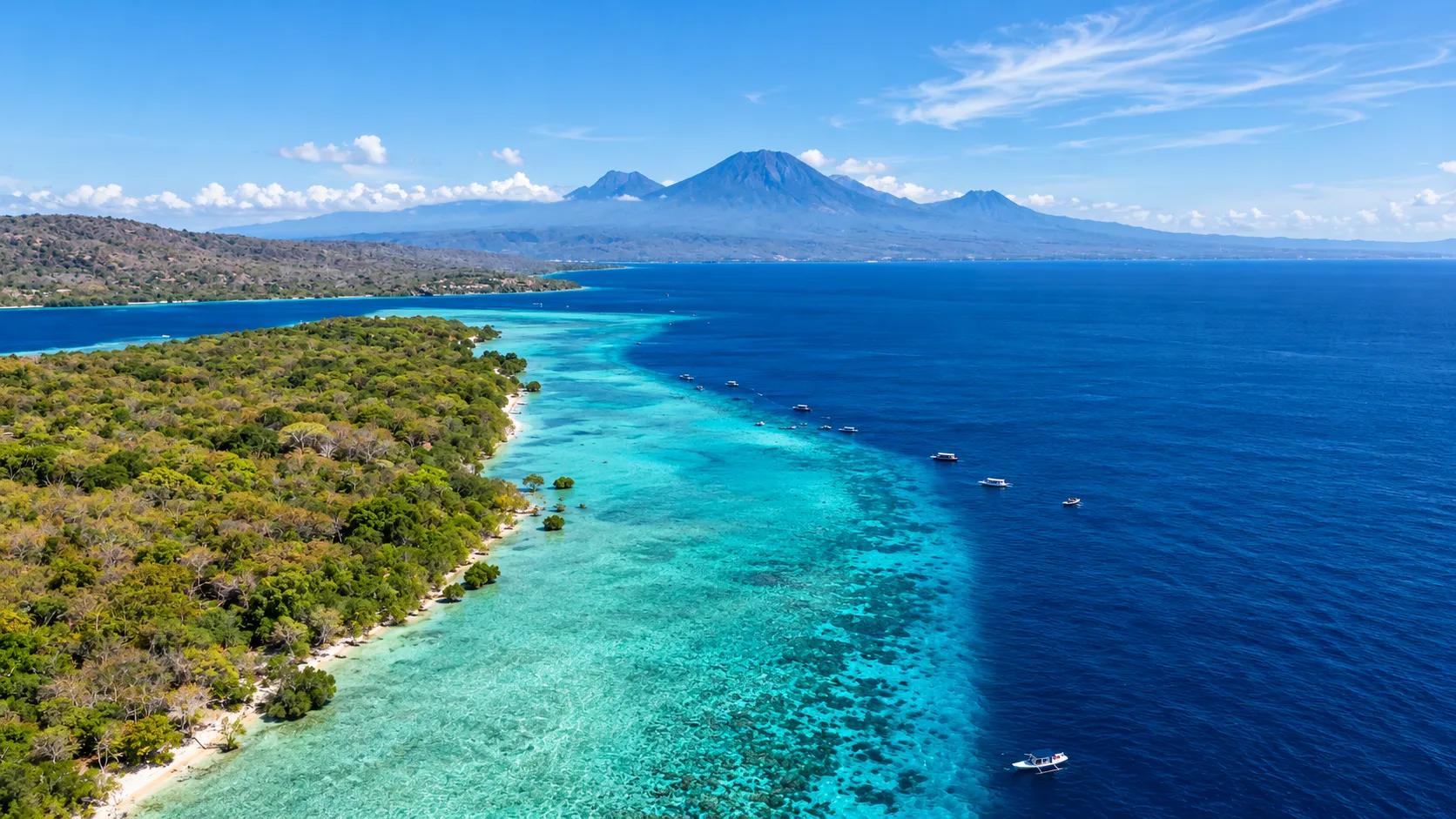 Aerial view of a north Bali diving reef with turquoise shallows, dive boats and volcanoes across the water