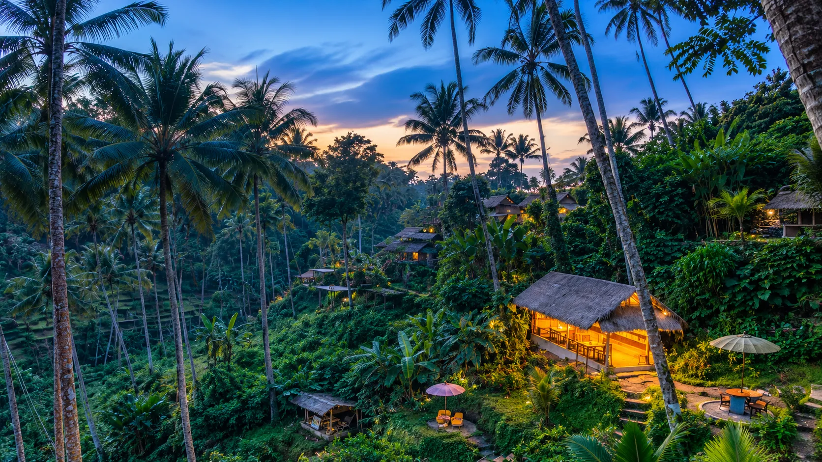 Thatched eco villas glowing at dusk among palms and rice terraces at a Bali eco resort in Ubud